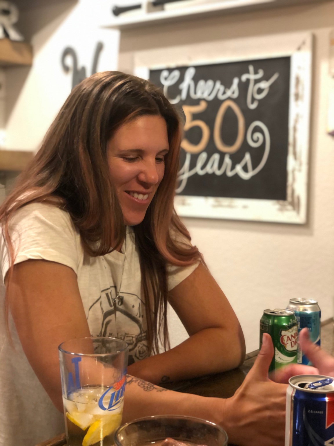 A guest smiling at the bar with a Cheers to 50 years sign behind her