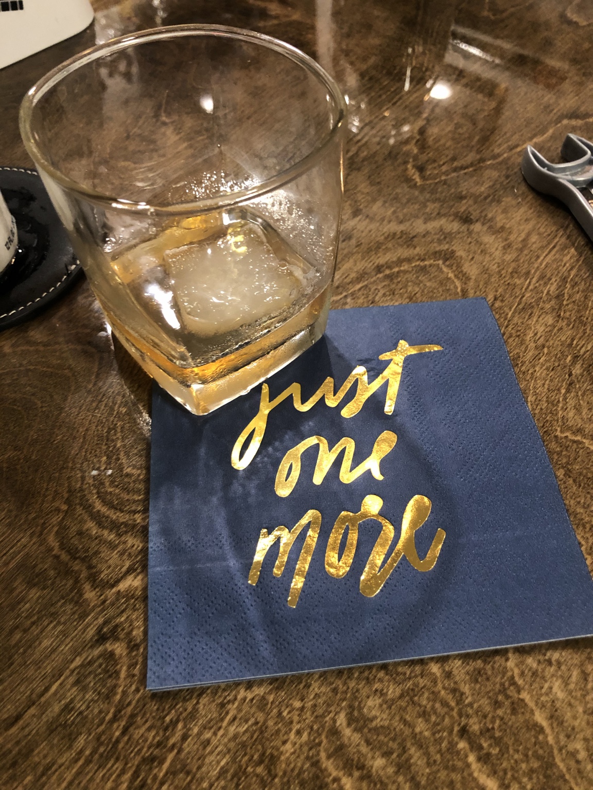 A drink on the wooden bar beside a navy napkin with gold lettering