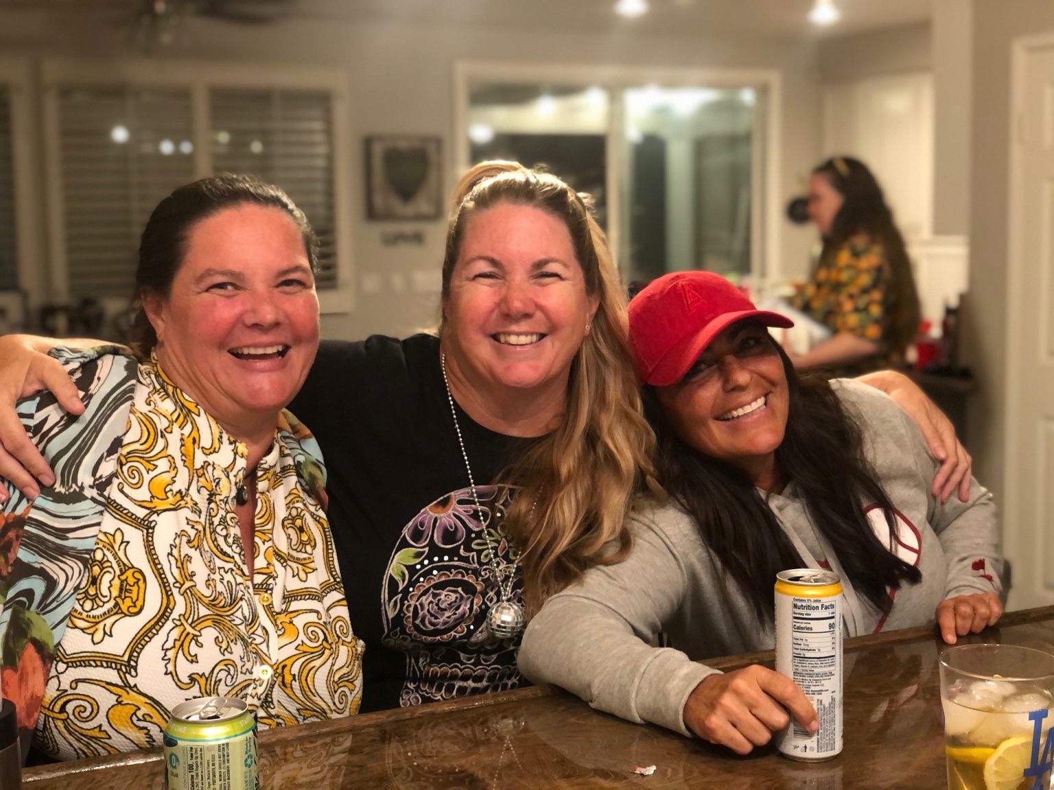 Three friends smiling with their arms around each other at the bar